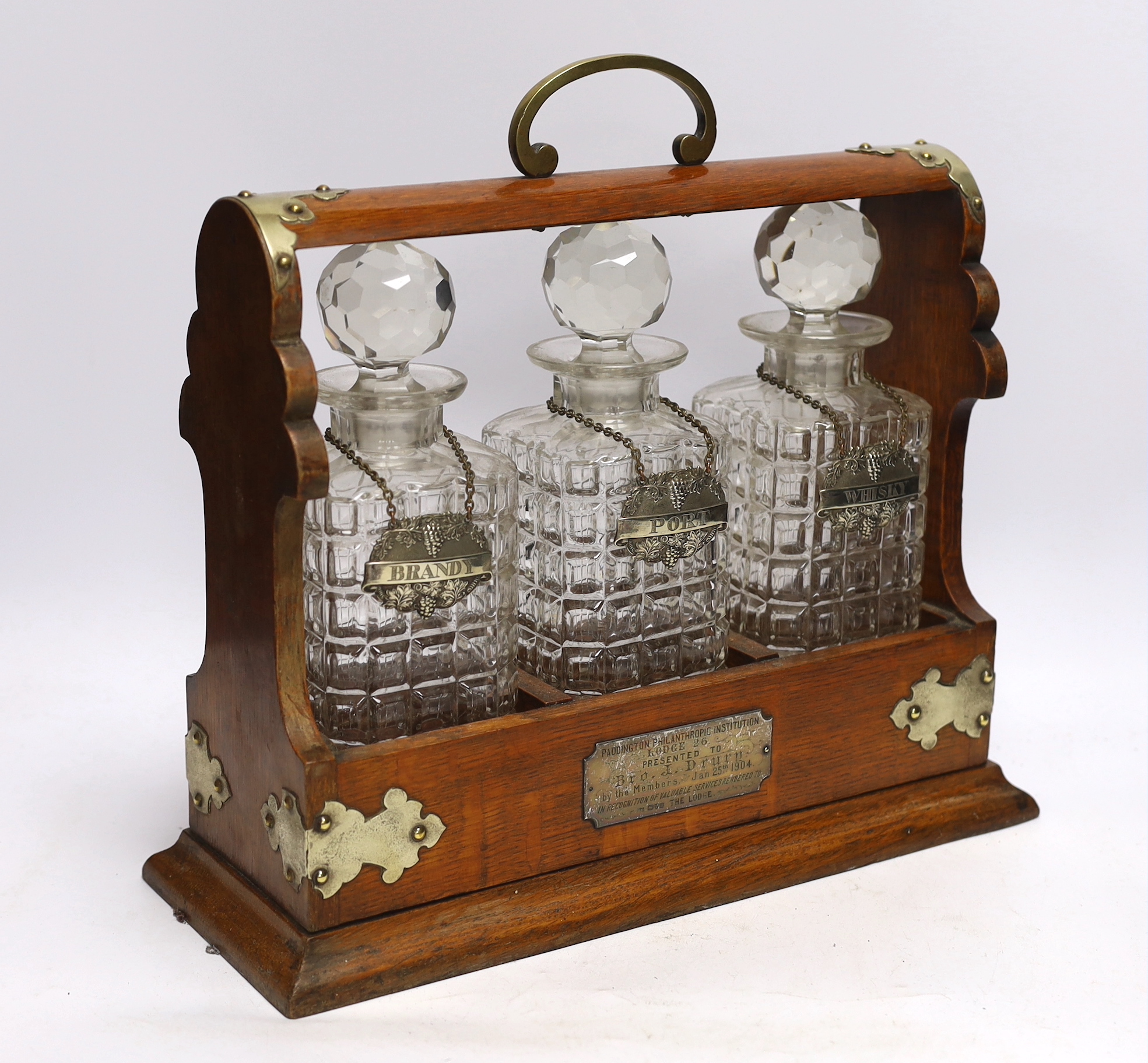 A three bottle tantalus with silver mounts and engraved Masonic presentation, 36cm wide